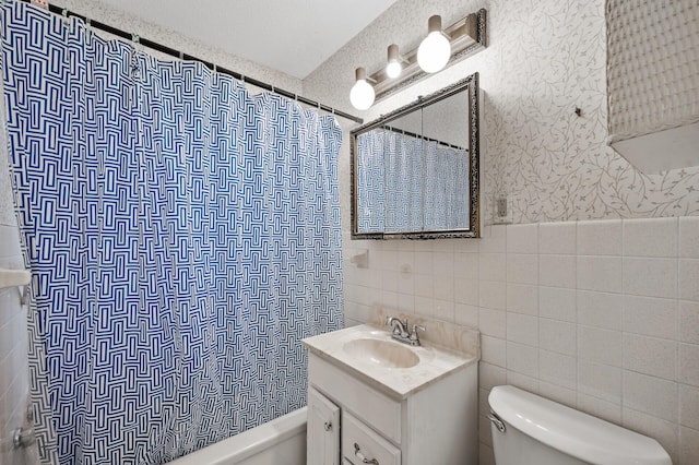 full bath featuring tile walls, wallpapered walls, toilet, vanity, and wainscoting