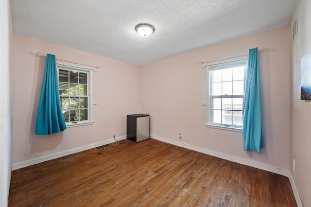 spare room with wood finished floors, a textured ceiling, healthy amount of natural light, and baseboards
