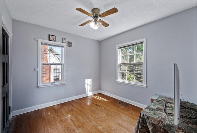 bedroom with multiple windows, wood finished floors, a textured ceiling, baseboards, and ceiling fan