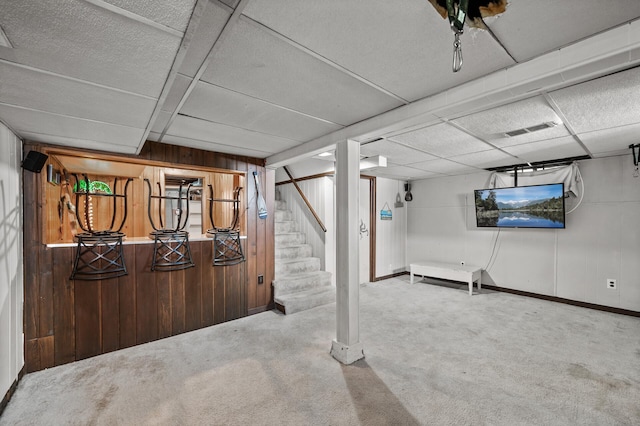 finished basement featuring carpet floors, wood walls, stairway, a drop ceiling, and baseboards