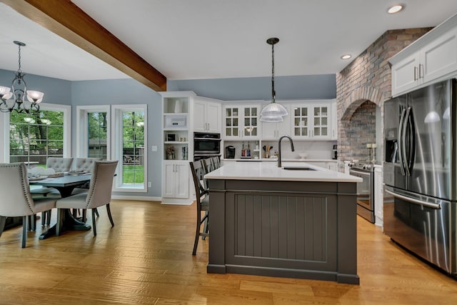 kitchen featuring appliances with stainless steel finishes, a sink, a chandelier, a center island with sink, and light countertops