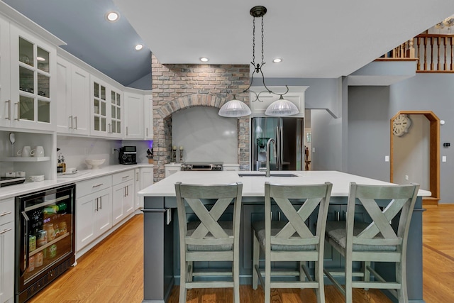 kitchen with beverage cooler, light countertops, black refrigerator with ice dispenser, light wood-style flooring, and an island with sink