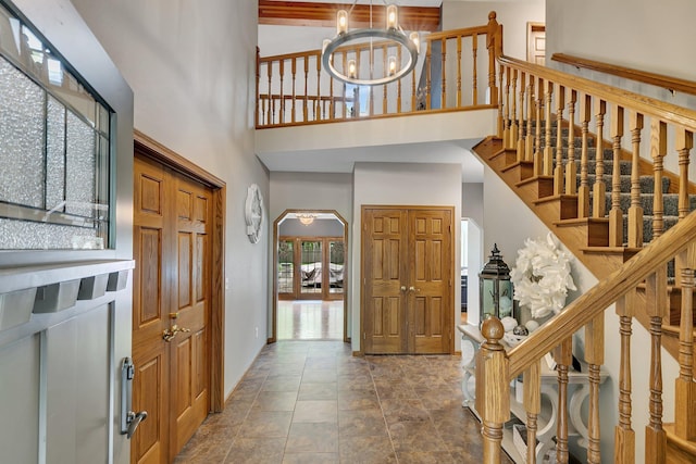 foyer entrance featuring a high ceiling, a chandelier, stone finish flooring, stairway, and arched walkways
