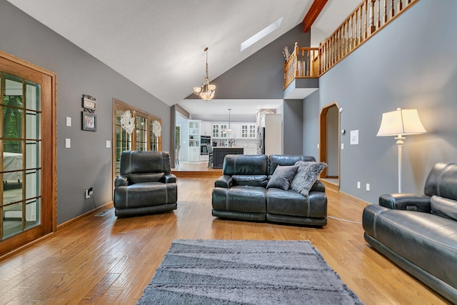 living room featuring wood-type flooring, arched walkways, a chandelier, baseboards, and beam ceiling