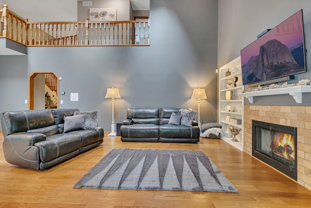living room featuring a towering ceiling, a fireplace, wood finished floors, and built in features