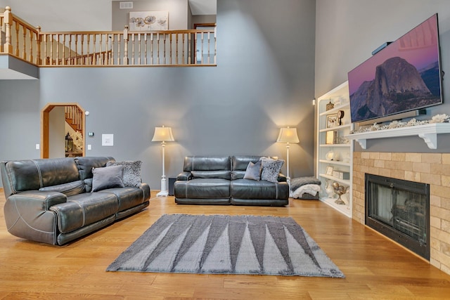 living area with a towering ceiling, a tiled fireplace, wood finished floors, and built in features