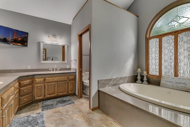 full bath featuring toilet, double vanity, a garden tub, and stone finish flooring