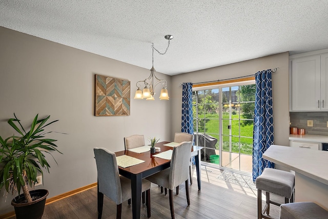 dining room featuring light wood finished floors, a chandelier, a textured ceiling, and baseboards