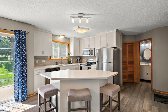 kitchen featuring stainless steel appliances, a sink, dark wood-style floors, a kitchen breakfast bar, and a textured ceiling