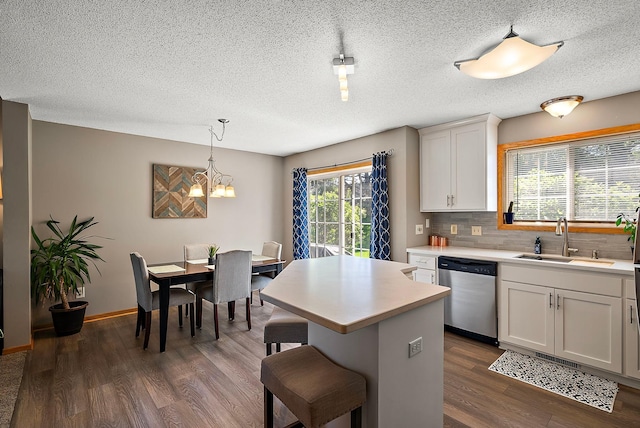 kitchen with stainless steel dishwasher, a sink, light countertops, dark wood-type flooring, and a chandelier