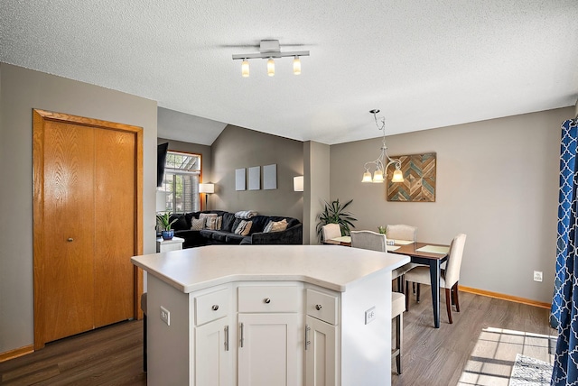 kitchen with wood finished floors, a chandelier, a kitchen island, white cabinetry, and light countertops