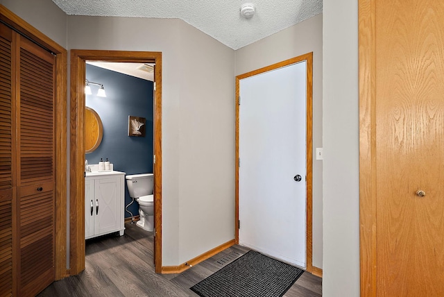 hall with wood finished floors, baseboards, a textured ceiling, and a sink