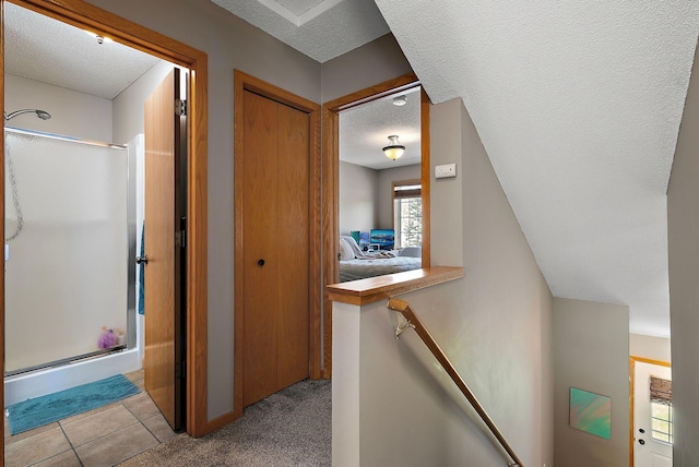 corridor featuring a textured ceiling, an upstairs landing, tile patterned floors, and carpet