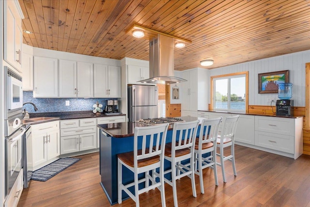 kitchen with stainless steel appliances, island exhaust hood, a sink, wooden ceiling, and dark countertops