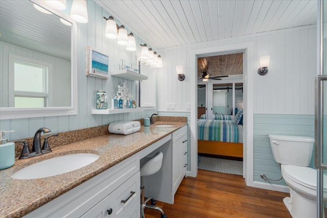ensuite bathroom featuring wooden ceiling, toilet, wood finished floors, double vanity, and wood walls