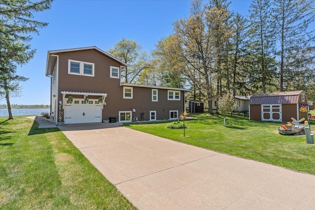 rear view of property featuring an attached garage, a storage unit, driveway, a yard, and a water view