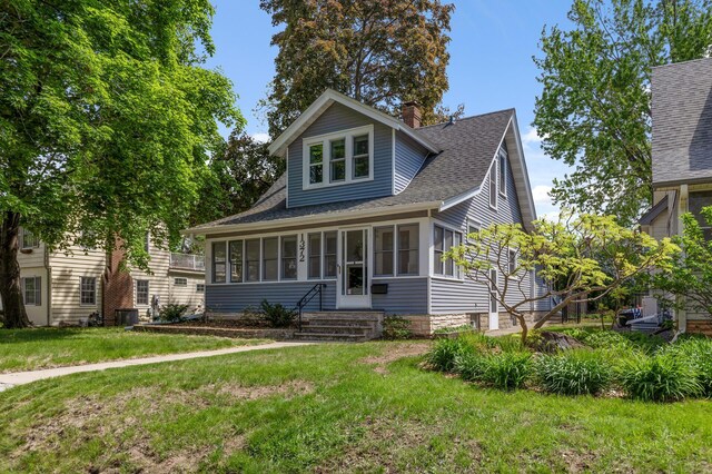 bungalow-style home with a sunroom, a chimney, a front lawn, and a shingled roof