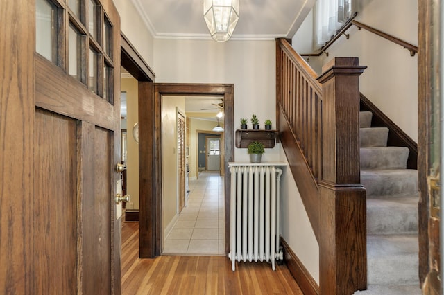 foyer entrance with radiator, crown molding, light wood finished floors, stairway, and baseboards