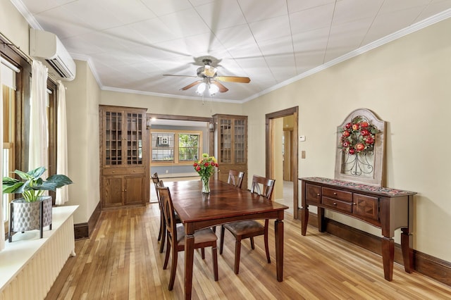 dining room featuring an AC wall unit, light wood finished floors, ceiling fan, ornamental molding, and baseboards