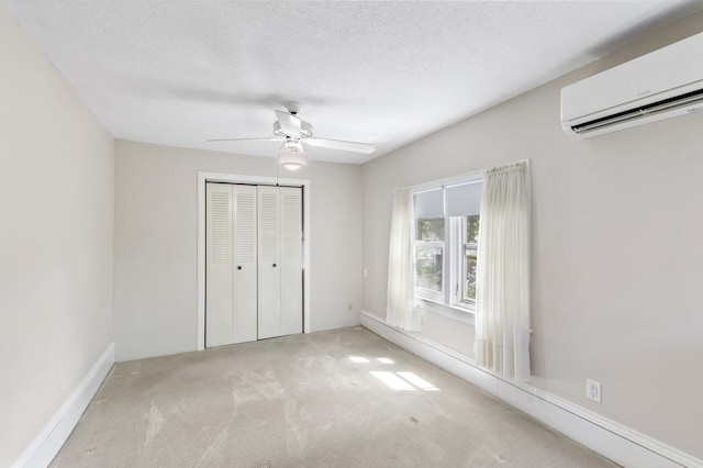 unfurnished bedroom featuring a wall mounted air conditioner, carpet flooring, a closet, a ceiling fan, and a textured ceiling