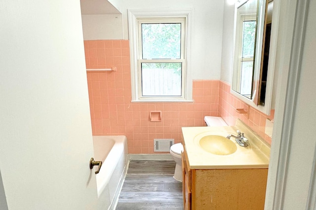 bathroom with tile walls, plenty of natural light, wood finished floors, toilet, and a tub