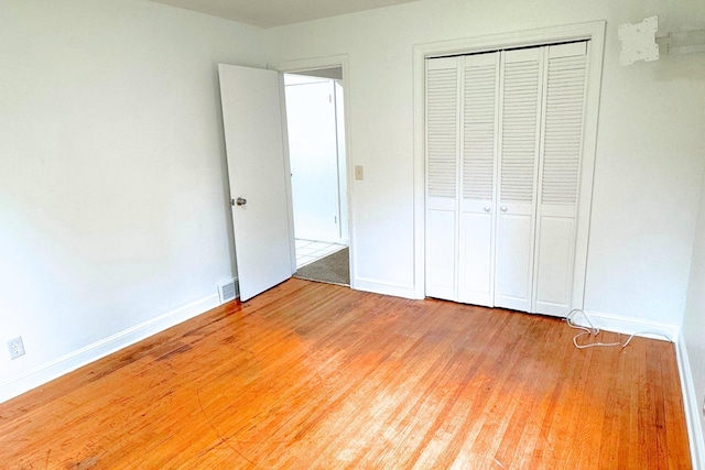unfurnished bedroom with wood finished floors, baseboards, and a closet