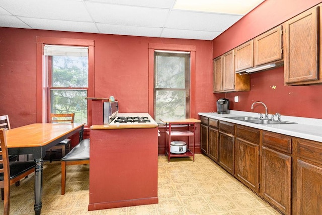 kitchen featuring a drop ceiling, a sink, light countertops, light flooring, and range