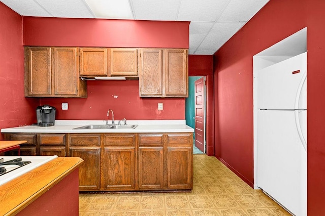 kitchen featuring white appliances, a sink, light countertops, a drop ceiling, and brown cabinetry