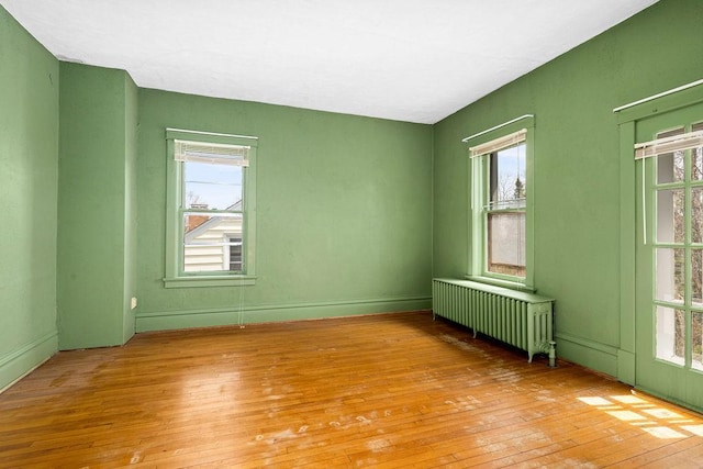 empty room featuring radiator, light wood-type flooring, and healthy amount of natural light