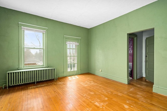 spare room with radiator heating unit, hardwood / wood-style flooring, and baseboards