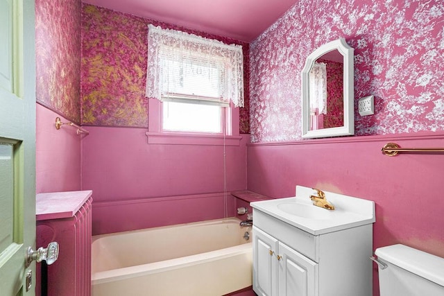 full bath with wallpapered walls, a bathtub, vanity, toilet, and a wainscoted wall