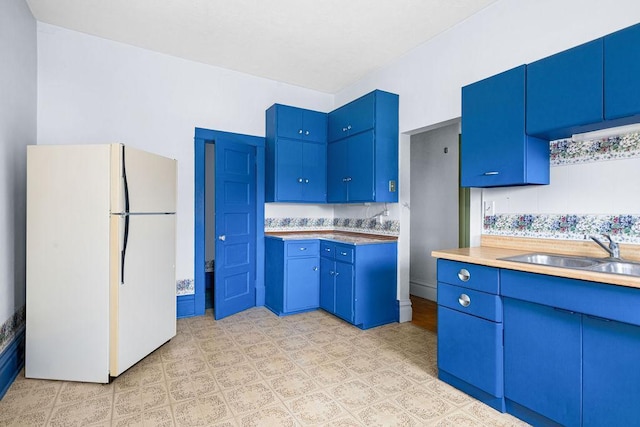 kitchen with freestanding refrigerator, blue cabinets, and a sink