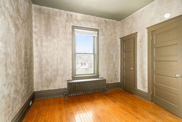 empty room featuring radiator, hardwood / wood-style flooring, and baseboards