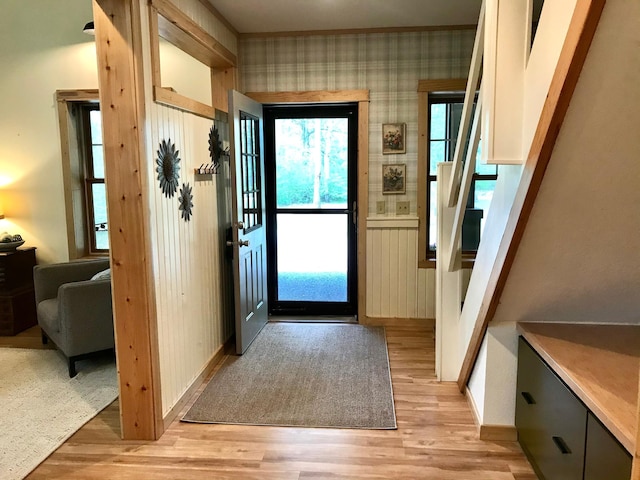 entrance foyer featuring light wood-style floors, stairs, baseboards, ornamental molding, and wallpapered walls