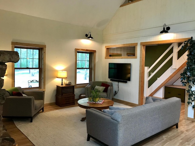 living area featuring high vaulted ceiling, wood finished floors, plenty of natural light, and stairs