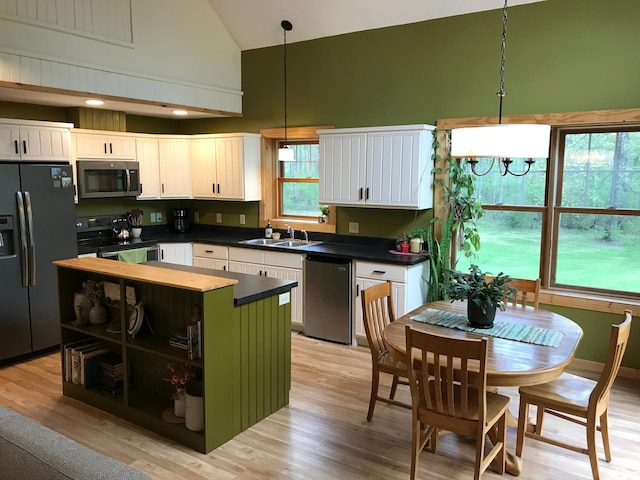 kitchen with stainless steel appliances, high vaulted ceiling, a sink, dark countertops, and white cabinets