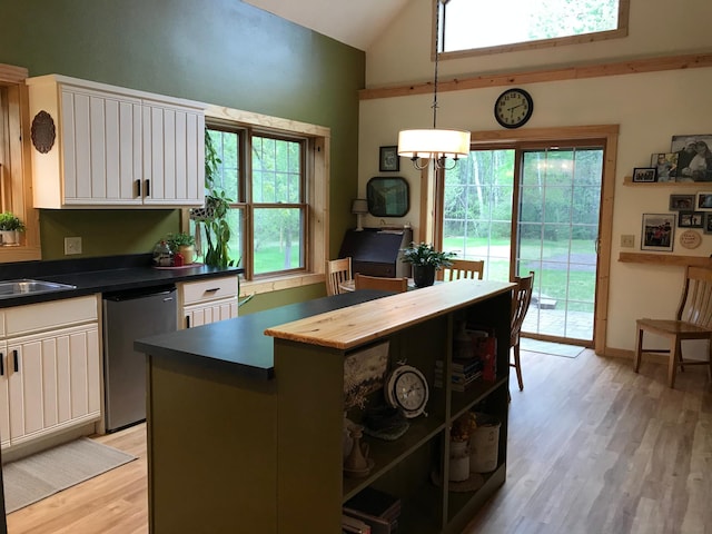 kitchen featuring dishwasher, light wood-style floors, dark countertops, white cabinetry, and high vaulted ceiling