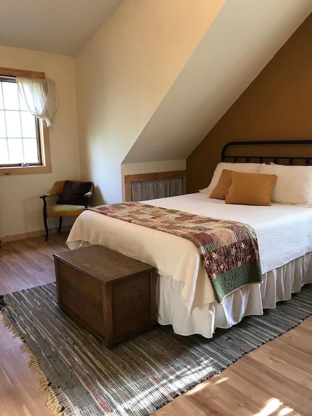 bedroom featuring wood finished floors, lofted ceiling, and baseboards