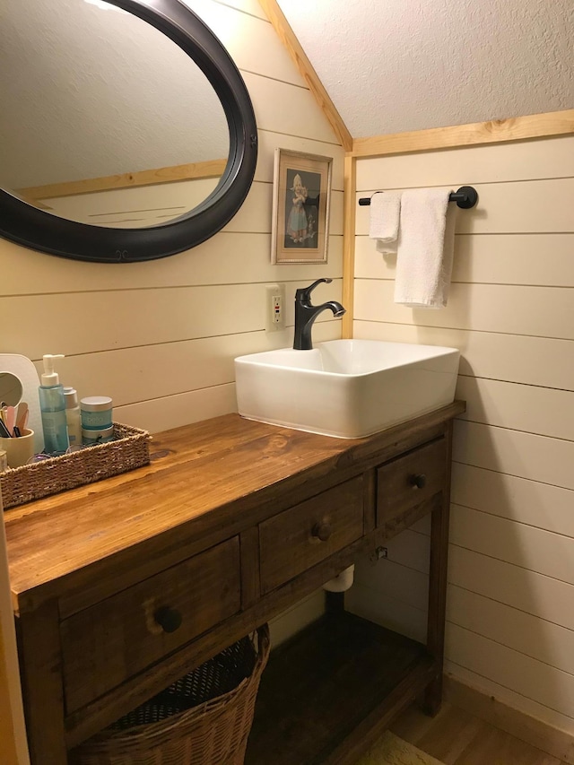 bathroom featuring vaulted ceiling, vanity, wooden walls, and a textured ceiling
