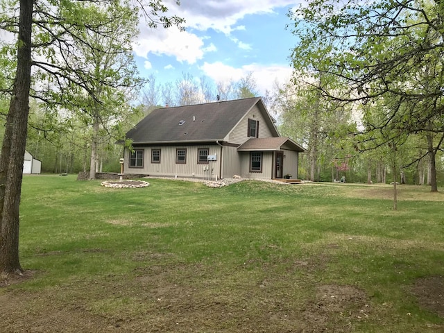 back of property featuring a lawn, roof with shingles, and an outdoor structure