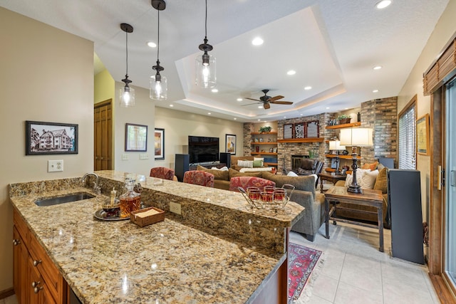 9378 Olympia Dr, Eden Prairie, MN 55347 - kitchen with ceiling fan, a fireplace, brown cabinets, a raised ceiling, and light stone counters