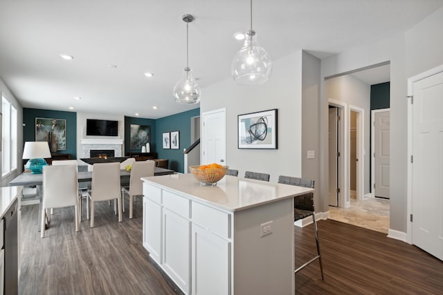 7581 Norway Ln, Lino Lakes, MN 55038 - kitchen featuring dark wood-style floors, a lit fireplace, a breakfast bar, white cabinetry, and a center island