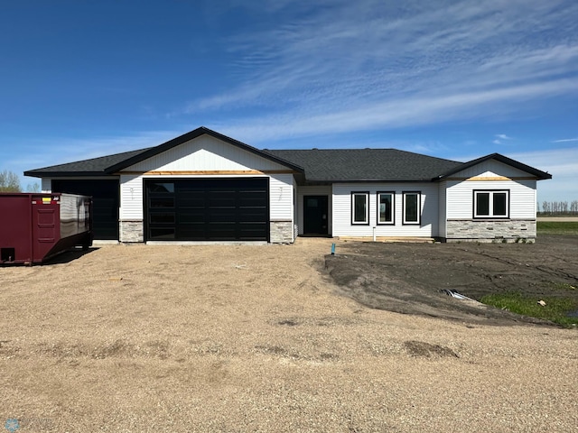 view of front of home featuring stone siding, a garage, driveway, and roof with shingles