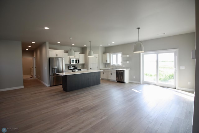 kitchen featuring appliances with stainless steel finishes, a center island, white cabinetry, open floor plan, and baseboards