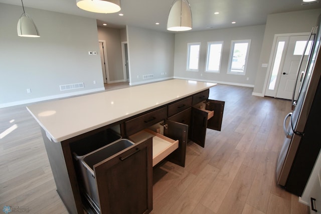 kitchen with freestanding refrigerator, open floor plan, a kitchen island, light wood-type flooring, and light countertops