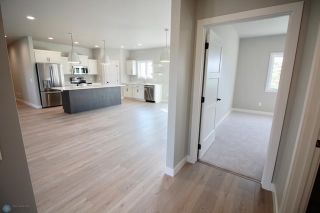kitchen with appliances with stainless steel finishes, white cabinets, a sink, light countertops, and light wood finished floors