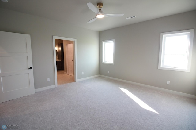 unfurnished bedroom with light colored carpet, baseboards, ensuite bath, and a ceiling fan