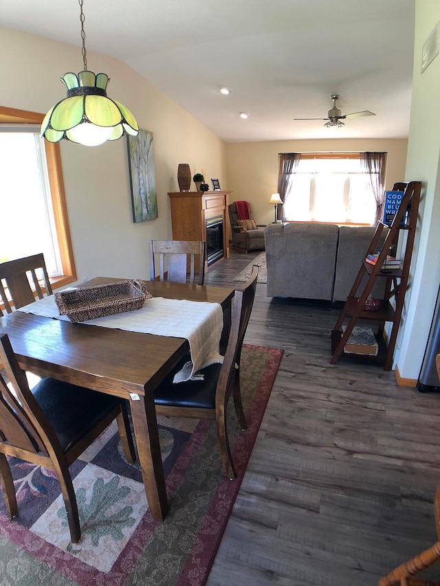 dining area featuring wood finished floors, a ceiling fan, vaulted ceiling, and a glass covered fireplace