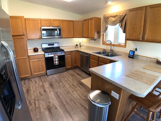 kitchen featuring appliances with stainless steel finishes, a sink, a peninsula, a kitchen bar, and vaulted ceiling