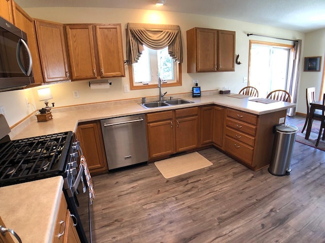 kitchen featuring dishwasher, a sink, black range with gas cooktop, a peninsula, and dark wood-style floors